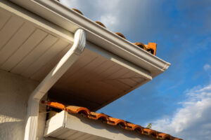 House corner with white planks siding and roof with steel gutter rain system and pipes installation